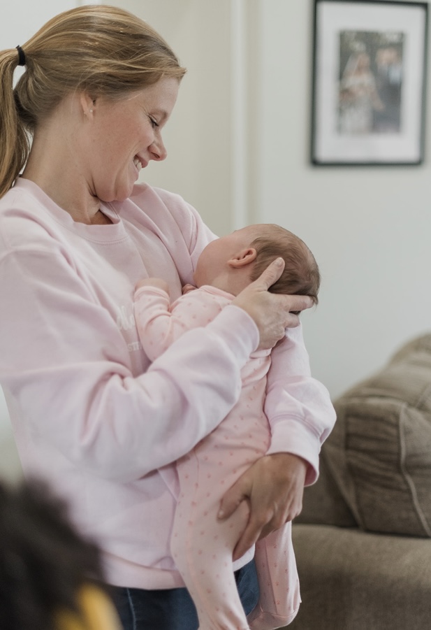 Kristin in a pale pink sweatshirt, holding a toddler close